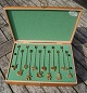 Georg Jensen Julepynt. 24 forskellige lysholdere i forgyldt messing, placeret i 
2 hylder i trækasse